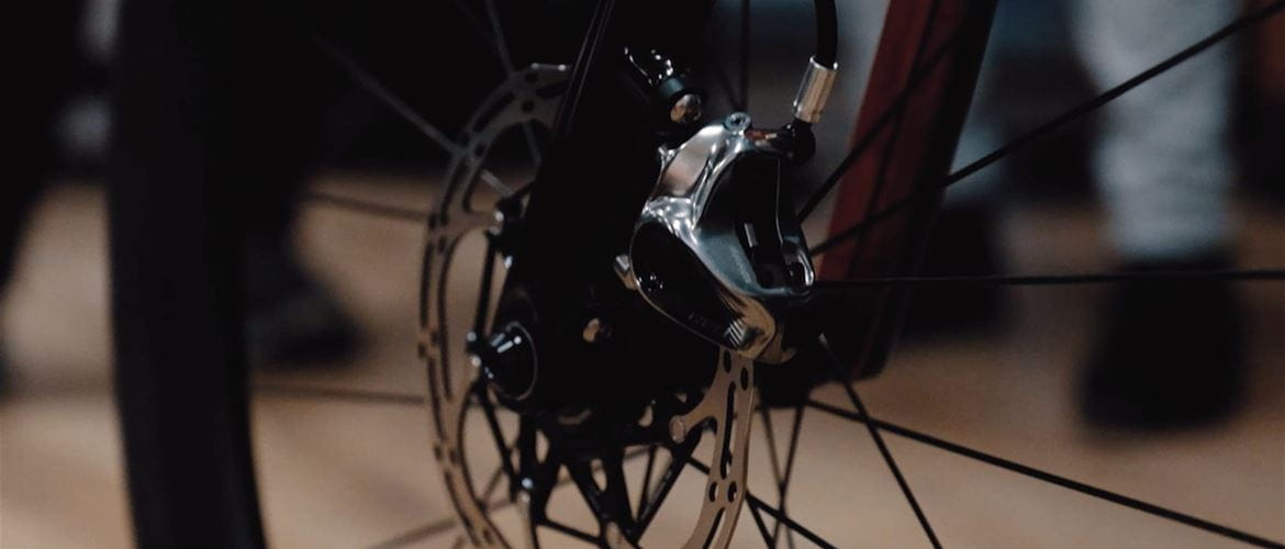 Close-up of bicycle disc brake with people's feet in the background