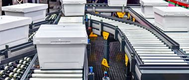 White plastic boxes on a roller conveyor in a warehouse environment
