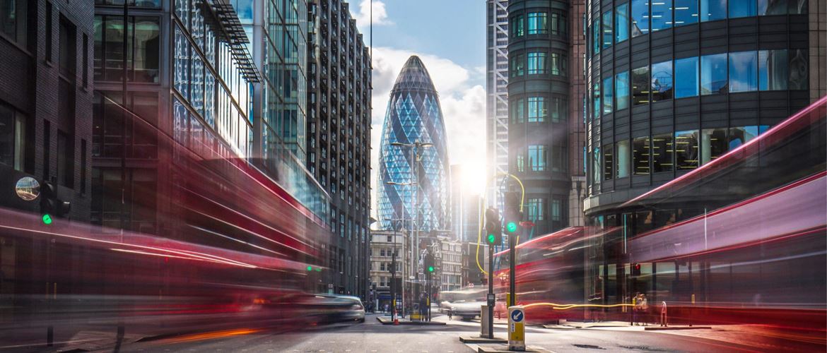 Long exposure shot, blurring red buses as they pass on both sides of a road in London's financial district