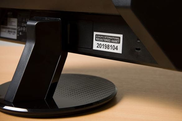 A black on white registered asset number label stuck on the bottom rear of a desktop computer display