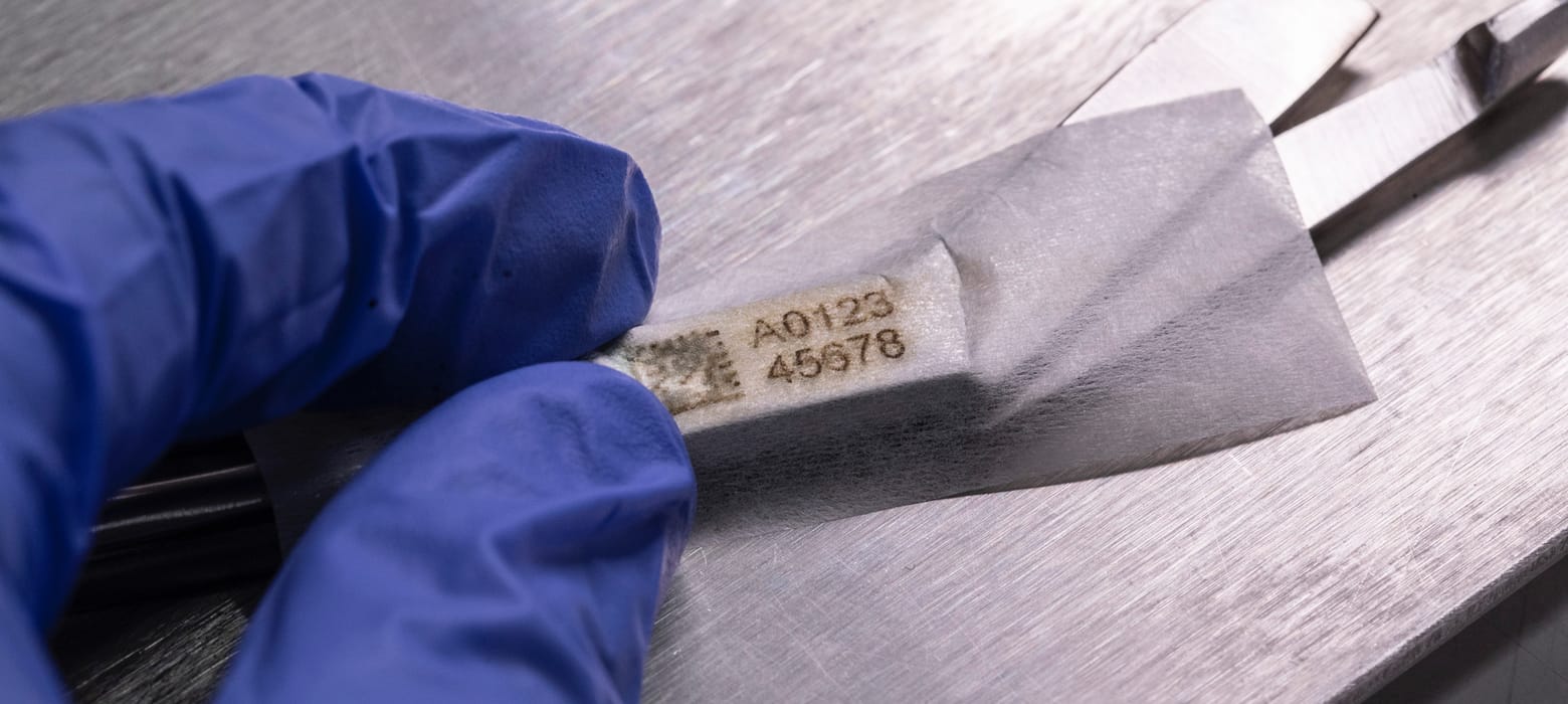 An industrial asset QR code stencil tape being applied to a brushed metal surface by someone wearing blue latex gloves
