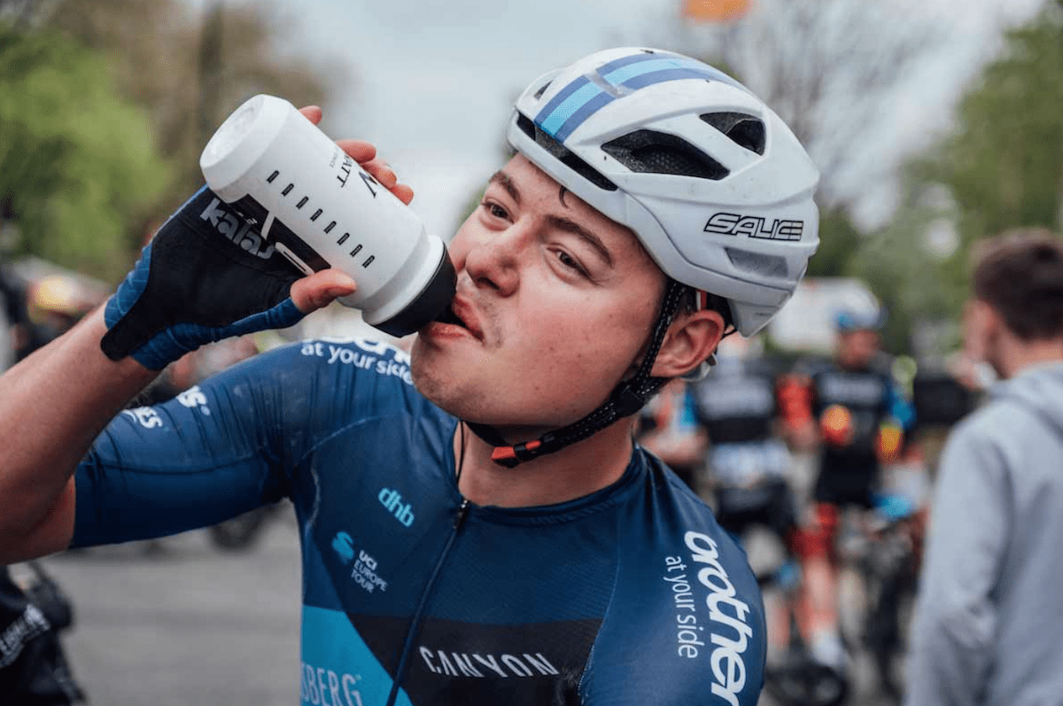 Racing cyclist, male, blue jersey, white helmet, drinking from white bottle