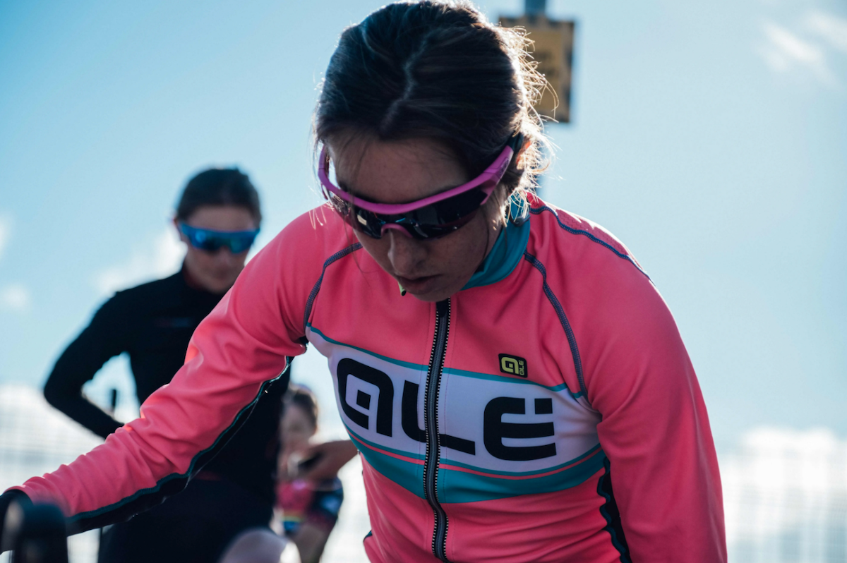 Female racing cyclist, pink jersey, dark hair, dark glasses, looking down