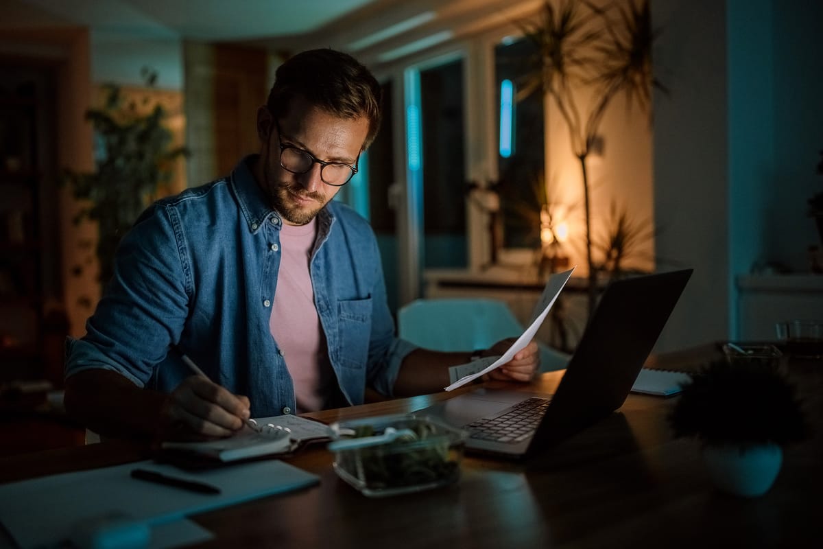 A man sat working at table in a softly lit home environment at night-time