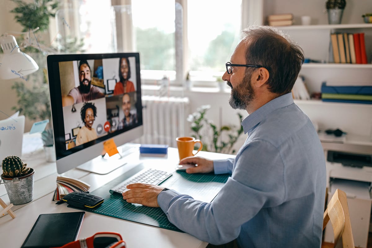 A businessman having a remote meeting with team members on a video call while sat at a desk in a home office environment