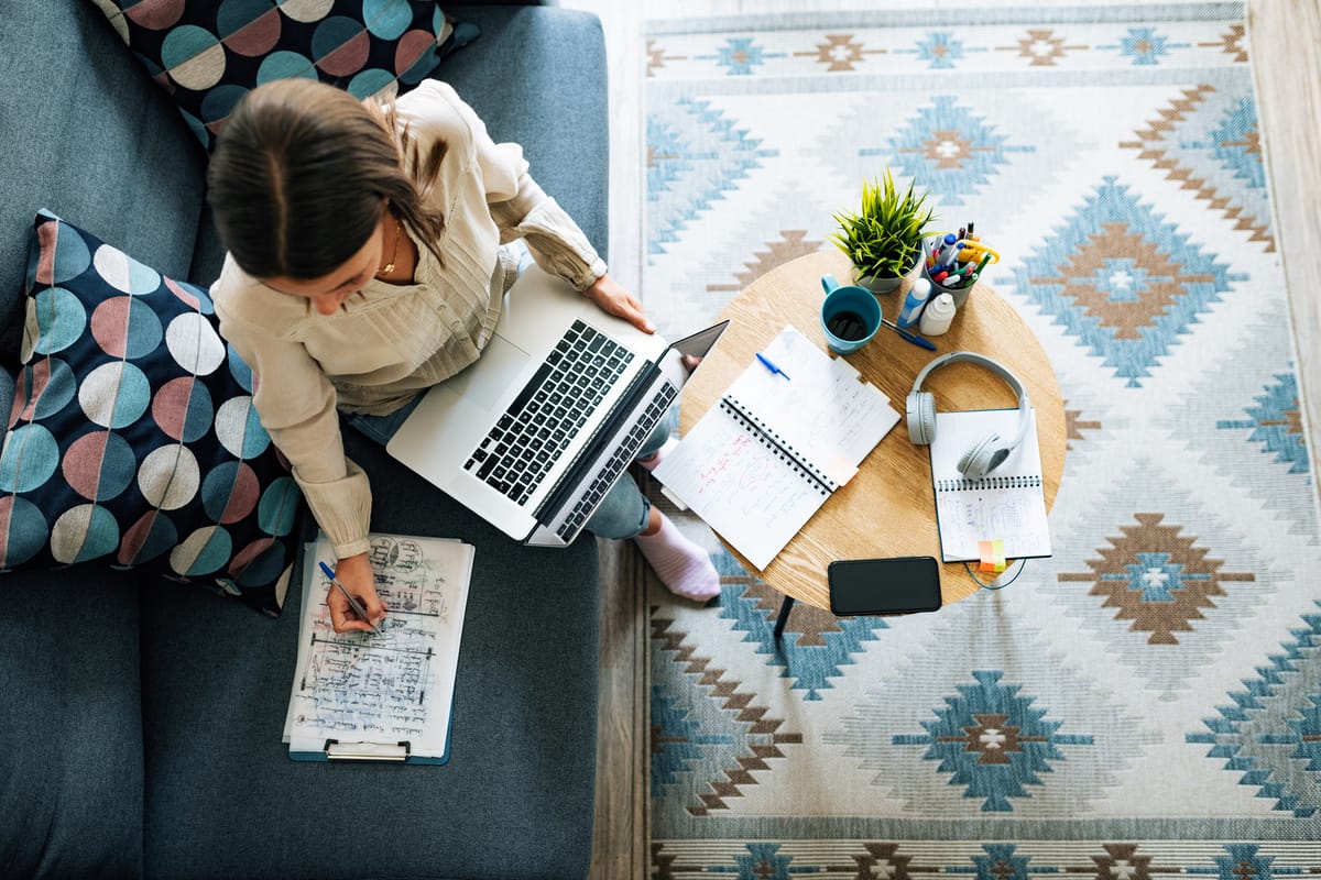 Overhead shot of a business woman using a notebook computer and making notes while sat on a sofa in a home environment