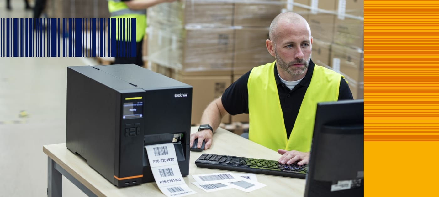 A male warehouse worker wearing a high visibility vest using a desktop computer to print barcode labels on a Brother industrial label printer