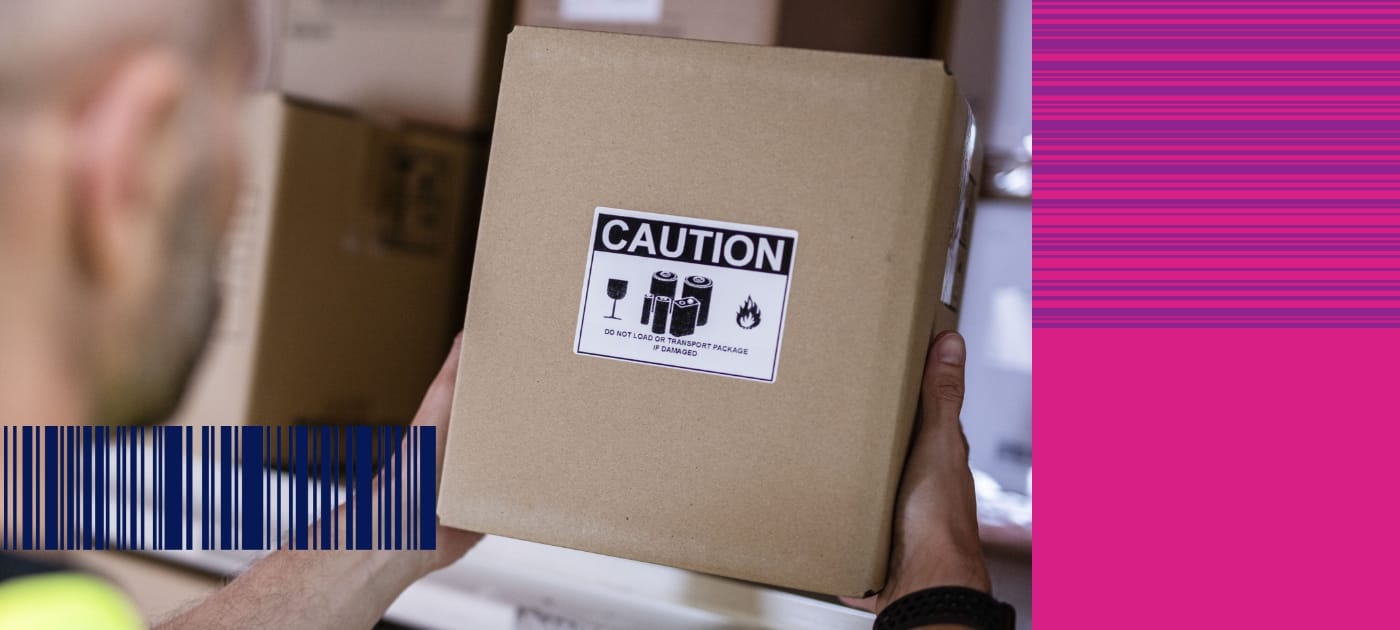 A warehouse worker lifting a brown cardboard box with a black and white caution label off a shelf