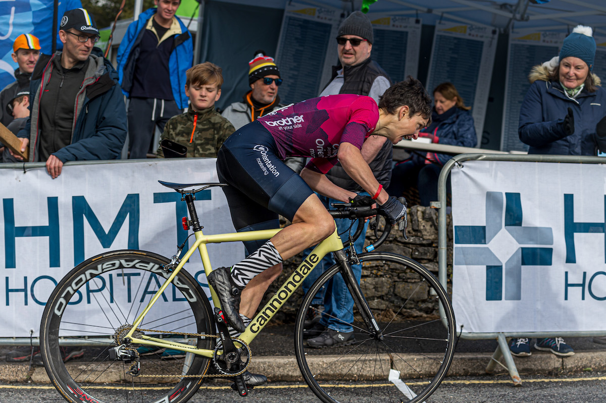 Female racing cyclist, red jersey, blue shorts, yellow bike, side view