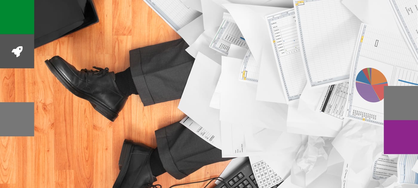 Overhead view of a businessman lying on a wooden floor, covered in papers with only his trouser bottoms and shoes visible