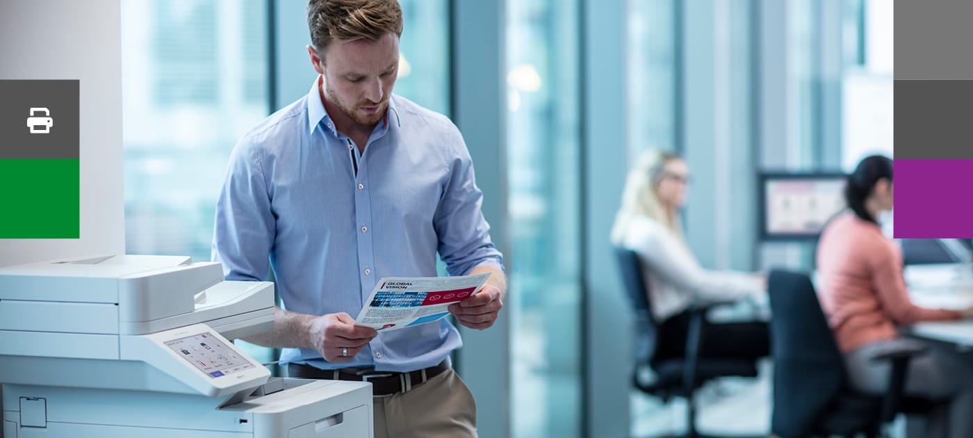 A businessman reading a document while stood next to a Brother colour laser printer in an office environment