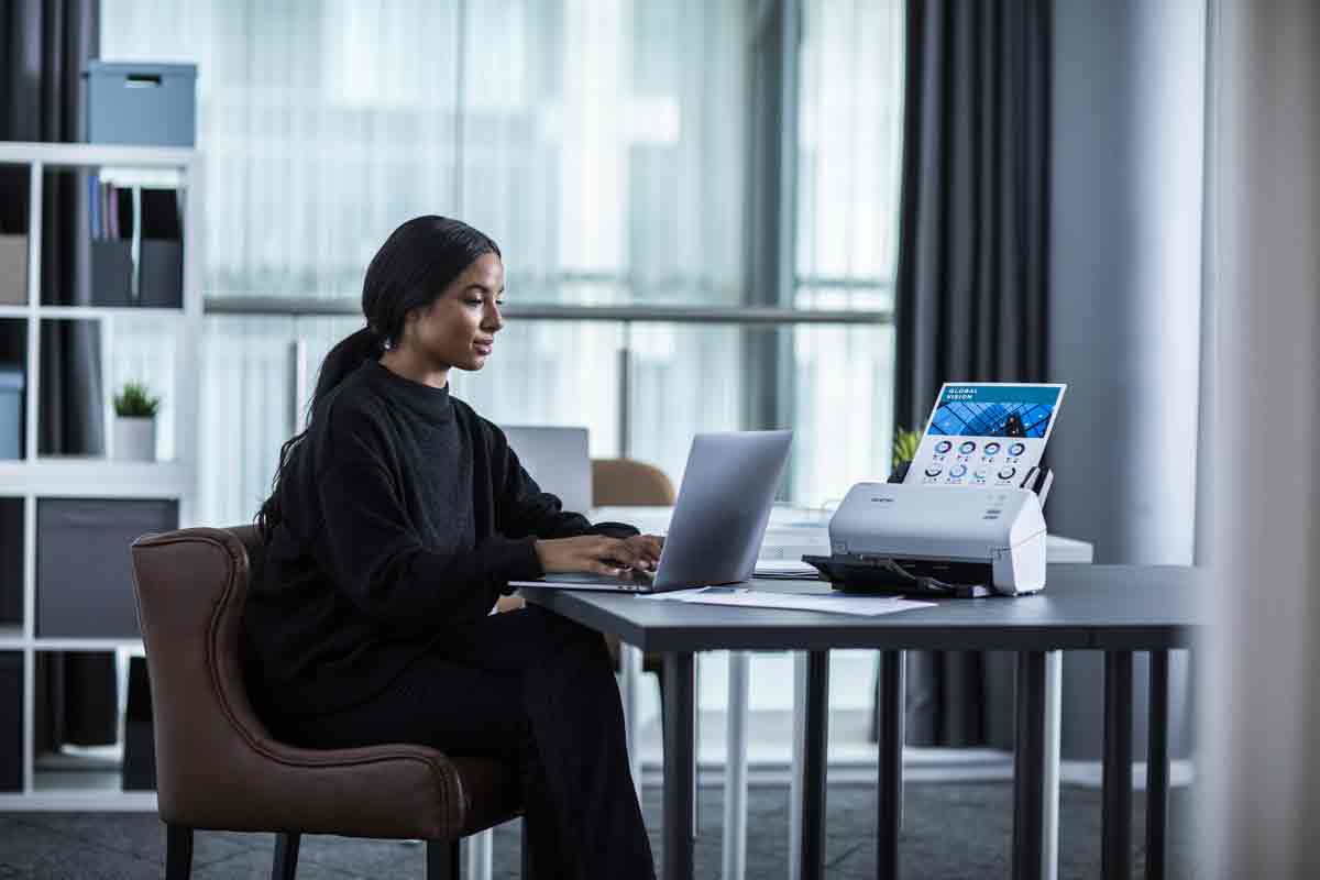 Lady sat at a desk with a Brother scanner on the desk