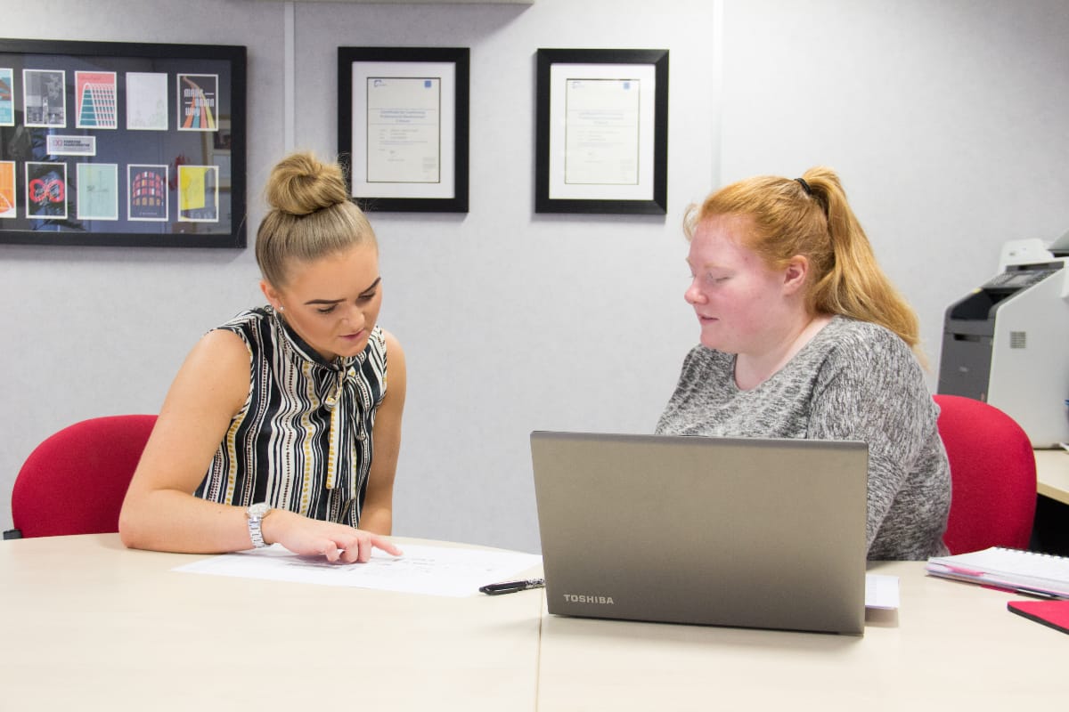 Sustainable Development Coordinator, Gemmer Crozier having a discussion with a colleague while sat at a desk in a meeting room