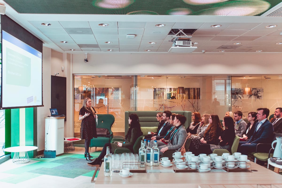 Sustainable Development Coordinator, Gemmer Crozier presenting to a conference room full of attendees with a table of refreshments in the foreground