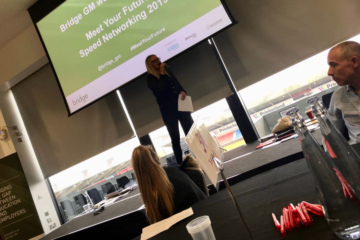 Sustainable Development Coordinator, Gemmer Crozier talking at a networking event while standing on a stage with a welcome slide projected behind her