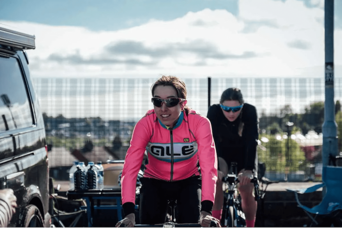Female racing cyclist, pink jersey, dark hair, dark glasses, smiling