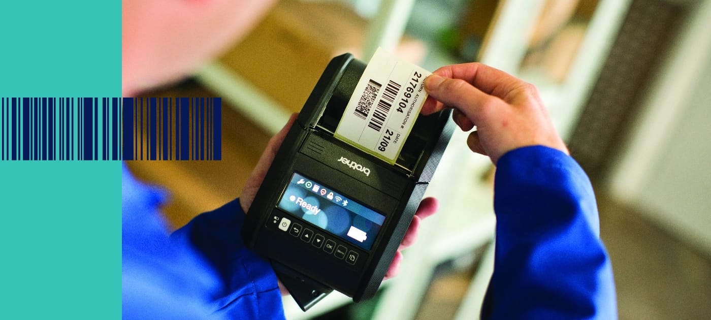 A person wearing a blue top removing a barcode label from a Brother RJ series mobile label printer