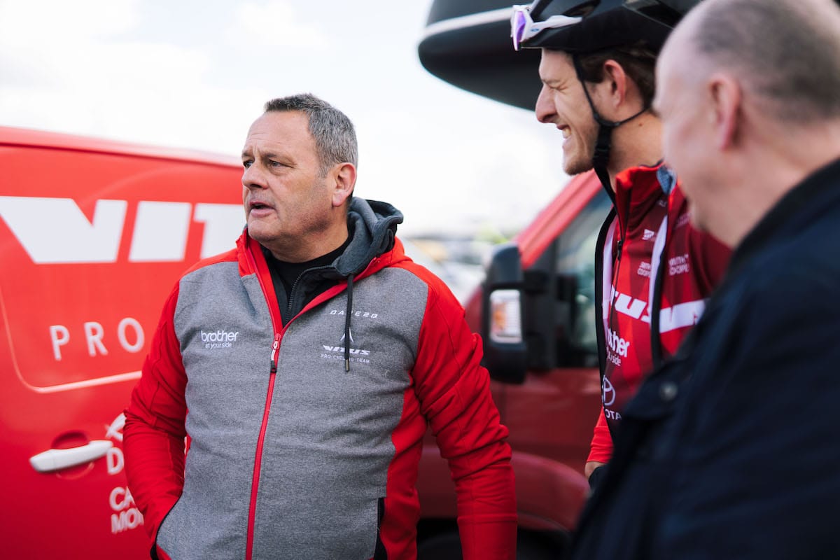 Mick Wright addresses the team in front of a red Vitus Pro Cycling Team van