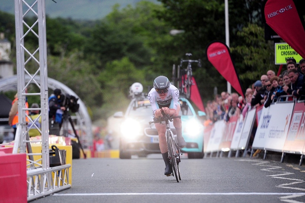 cyclist crosses the line with support vehicles behind