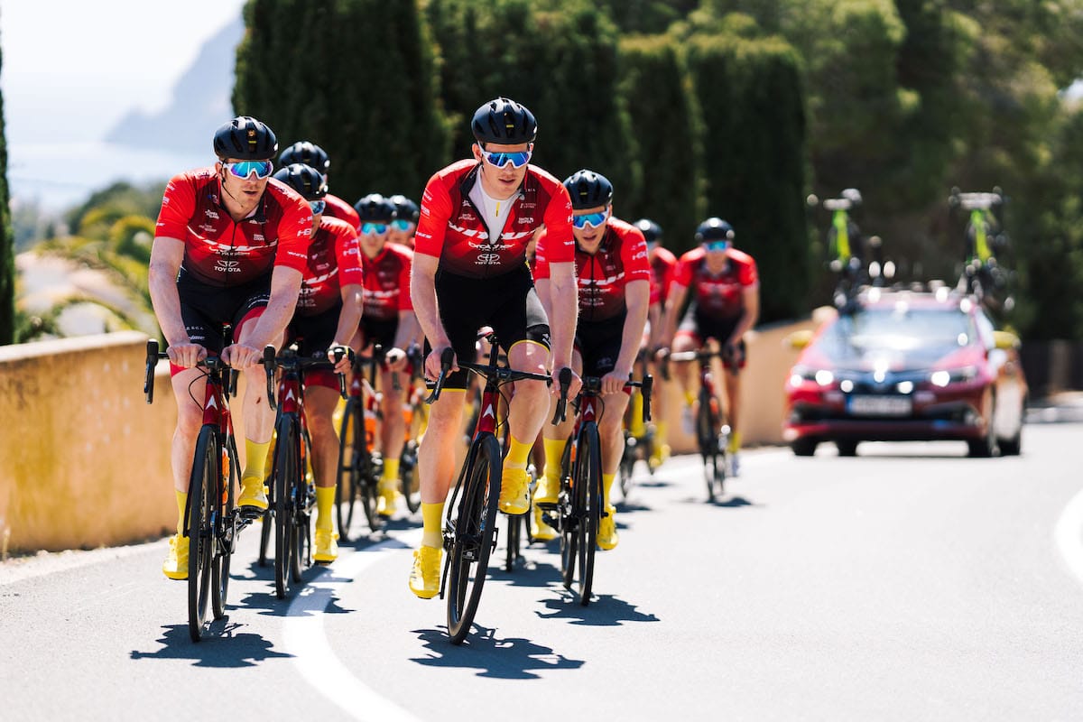 Cyclist Ed Clancy leading two rows of team mates with a support vehicle following at the rear