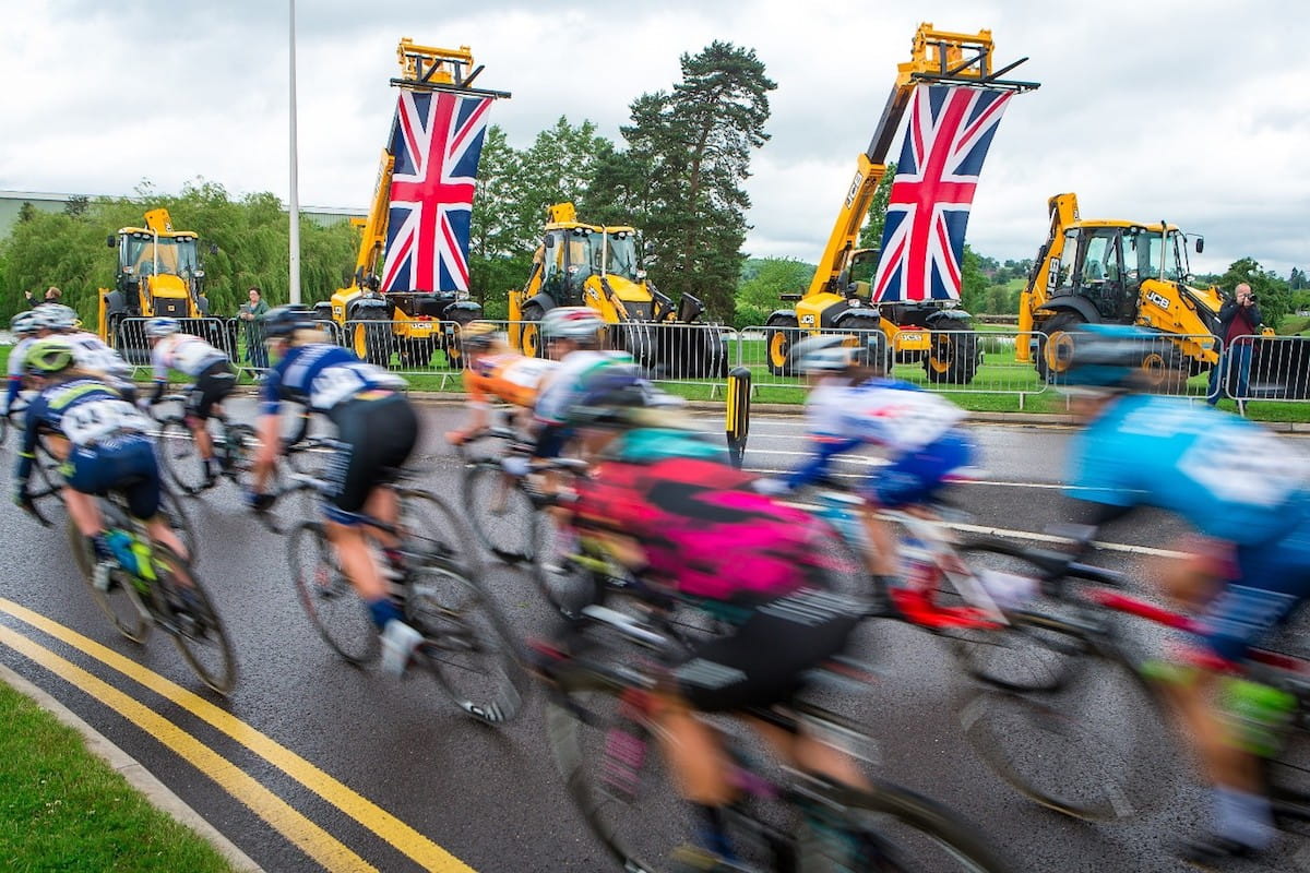cyclists speed round corner with JCB's displaying the union flag