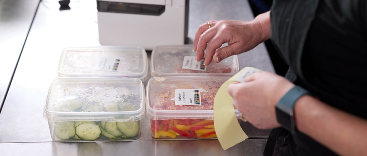A woman applying some printed day dot labels to 4 separate food containers 