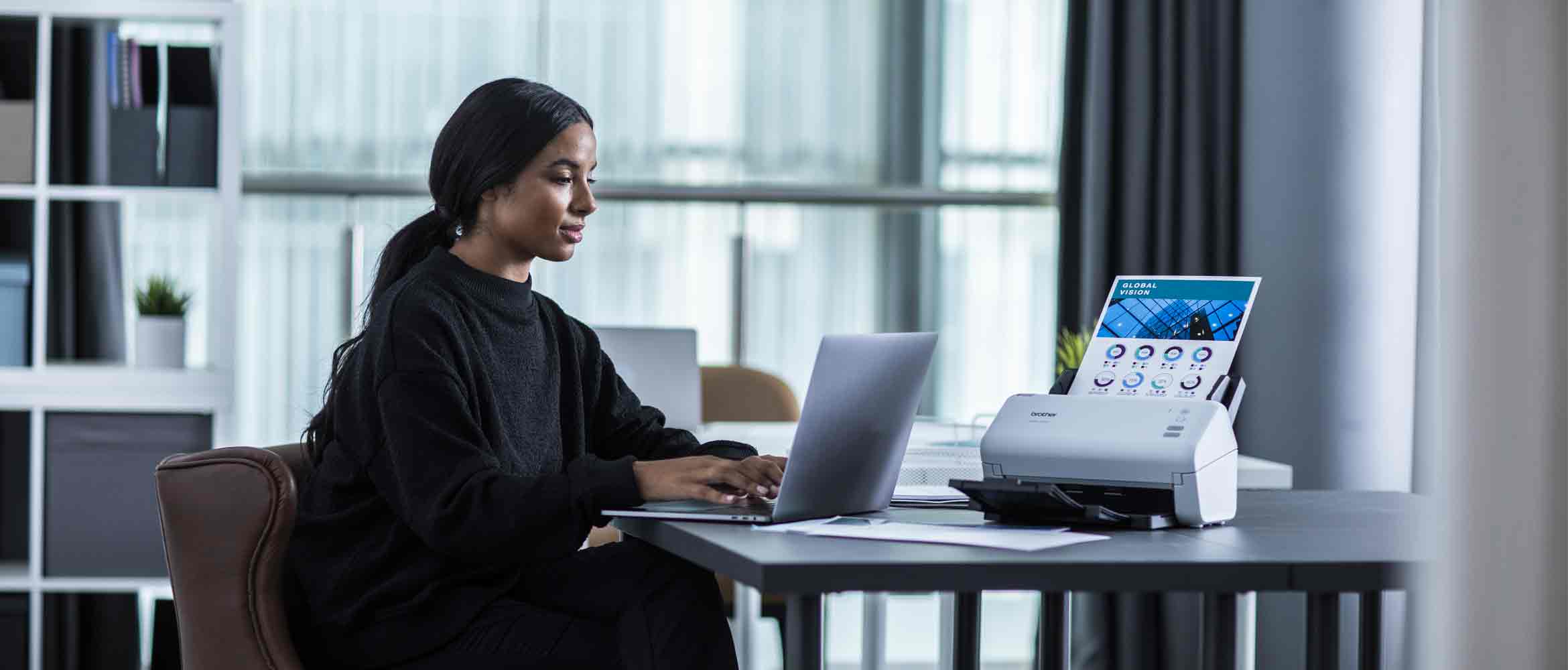 Lady sat at a desk working on a laptop with a Brother scanner on the desk