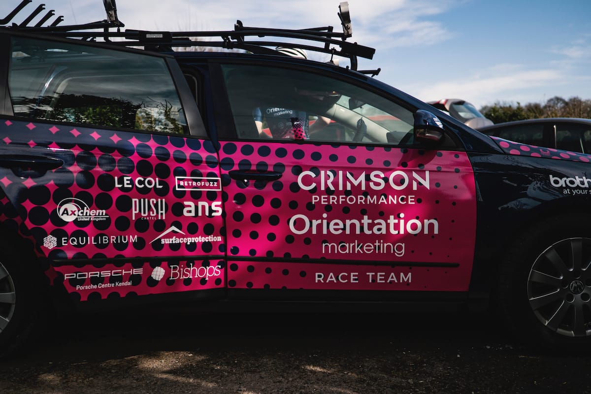 Side view of a black Crimson Performance race team support vehicle with pink sponsor livery
