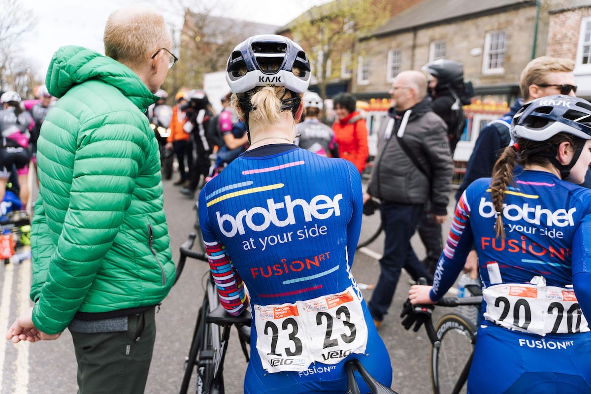 The backs of two cyclists wearing Brother UK-FusionRT team colours preparing to race