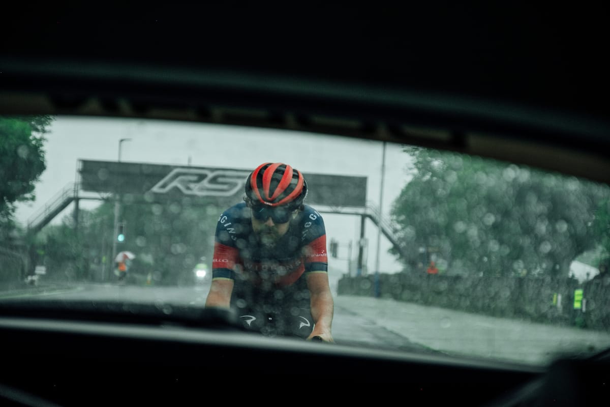 A view of cyclist Ben Healy through the rear window of a Neutral Service race support vehicle as he's riding behind