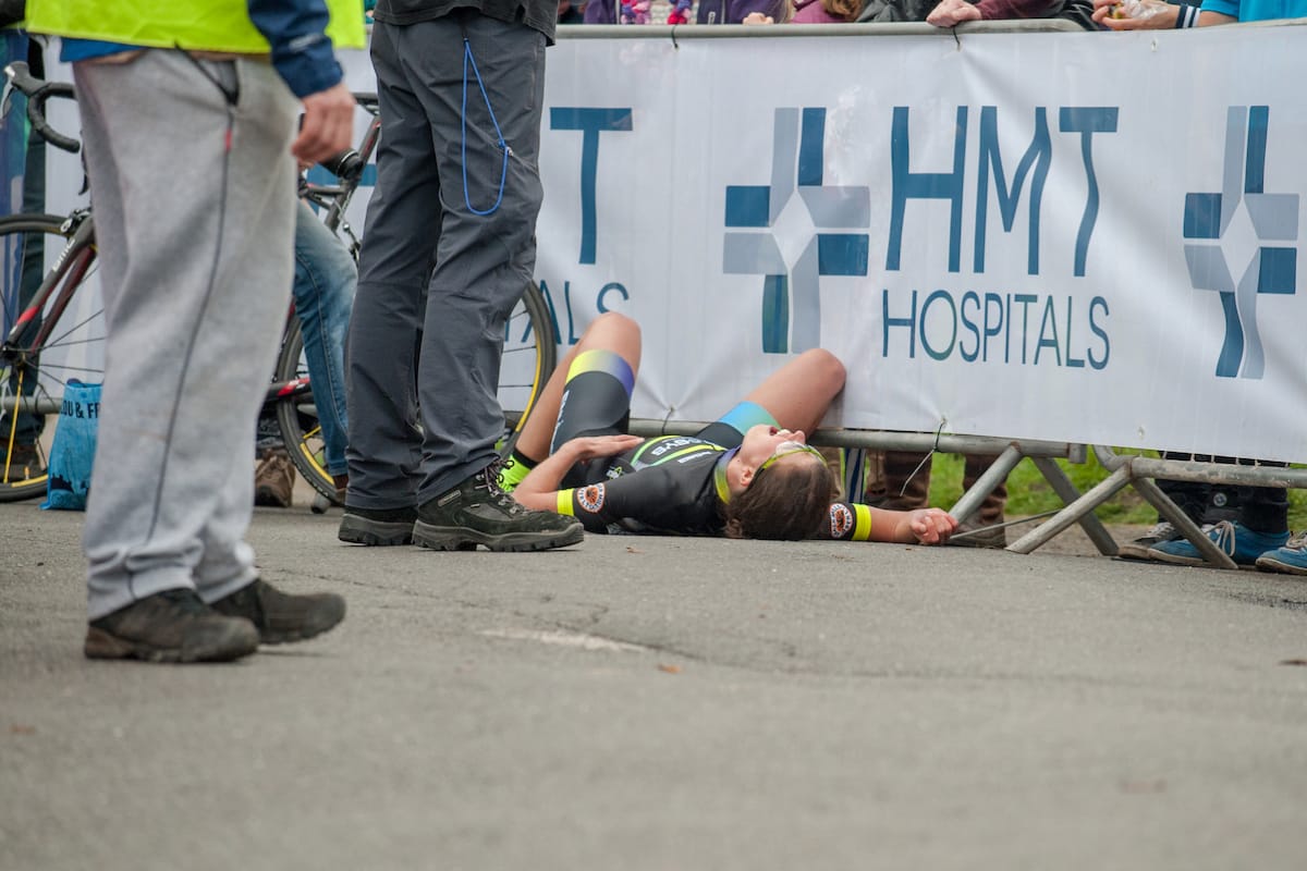 A cyclist collapses in front of the spectator barrier at a hill climb