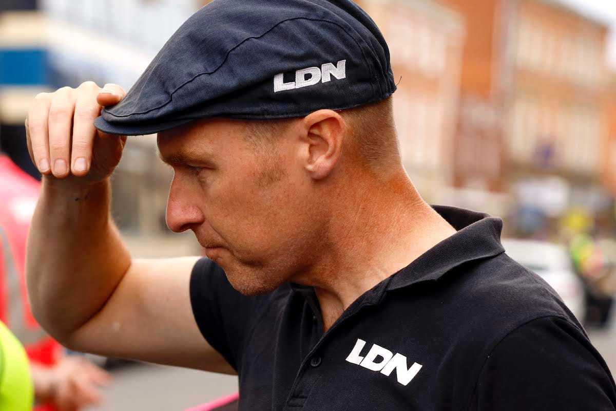 Side view of team manager Ian Watson holding the front of his flat cap