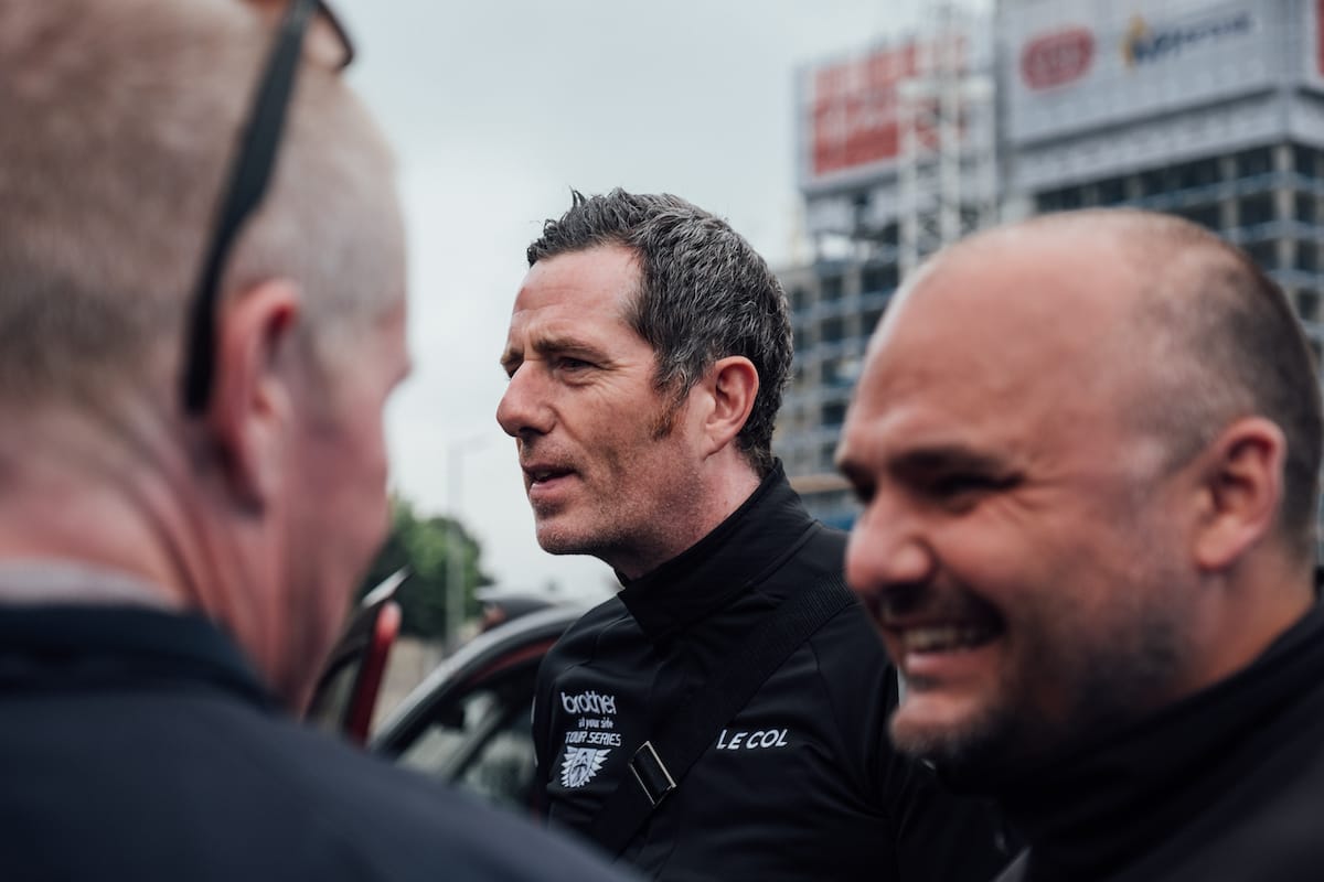 Simon Howes and Phil Jones MBE smiling and talking to people who are partially out of shot with a building under construction in the background
