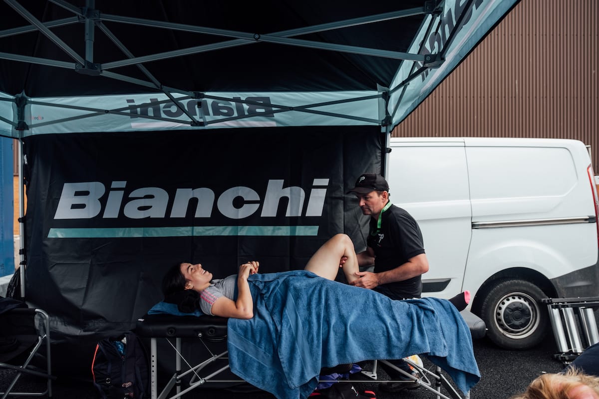 Soigneur Phil Holloway helping a cyclist warm up while they are lying on a treatment table under a Bianchi branded gazebo