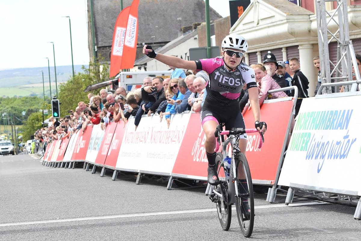 Cyclist punching the air while crossing the finishing line with spectators cheering her on in the background