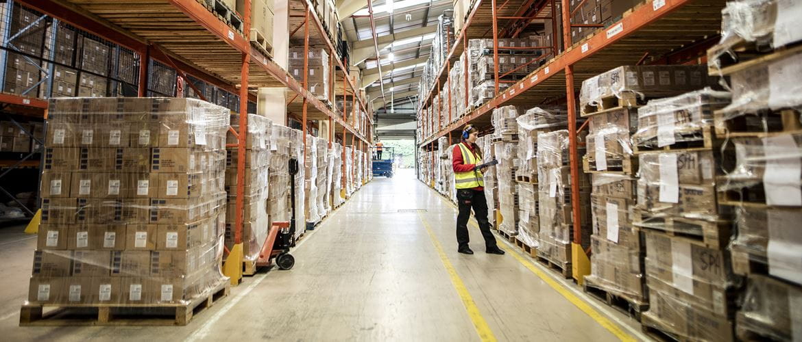 A woman in a high visibility jacket working in a warehouse full of boxes