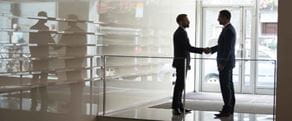 Silhouette of two businessmen shaking hands in office lobby. Male business professional executive colleagues standing near doorway of modern building, handshake.