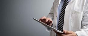 Close-up of doctor wearing white coat entering information into a tablet device