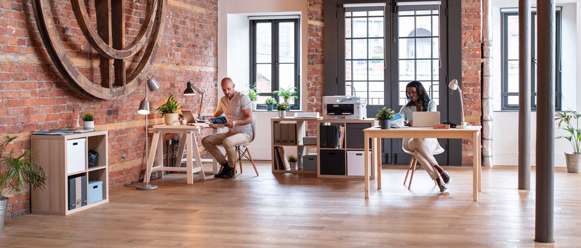 Male and female colleagues working at desks in an exposed brick open plan office environment