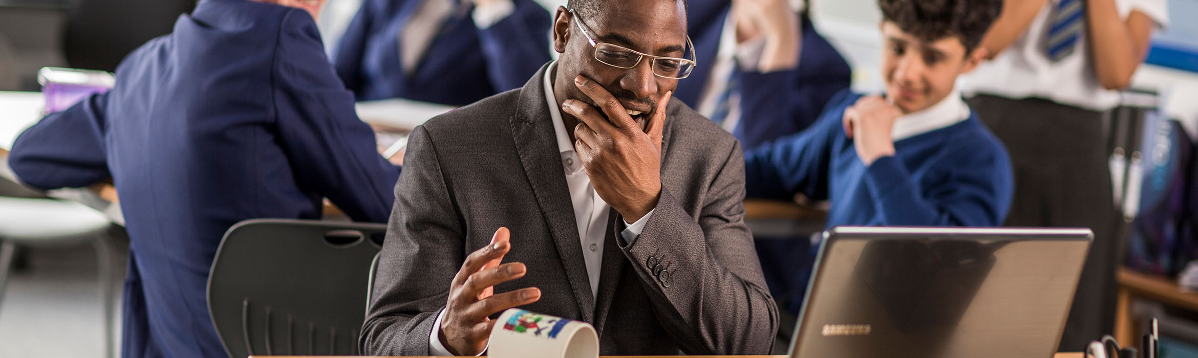 Man holds his face looking down at a mug in his hand in front of a computer screen
