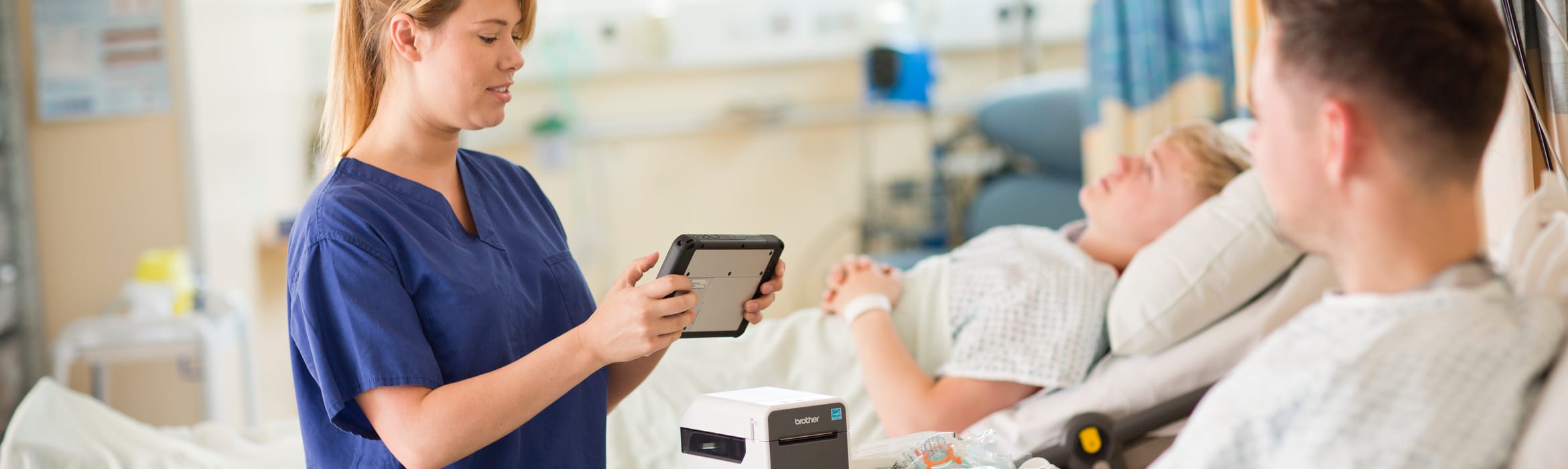 A female nurse printing an identification wristband for a male patient from a tablet device to a Brother label printer in a hospital ward