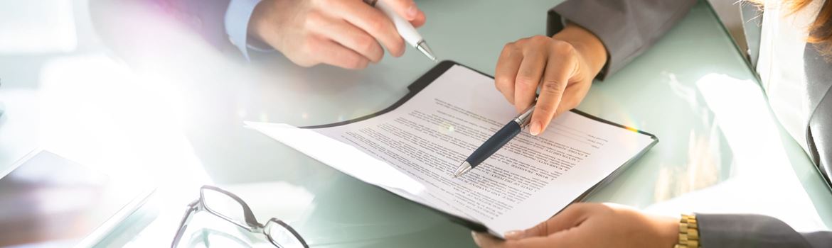 Two solicitors sitting at a table, each holding a pen while pointing to a section in a document