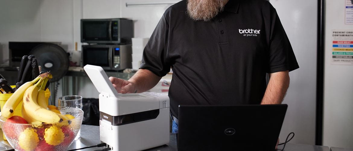 A man using a Brother label printer in kitchen