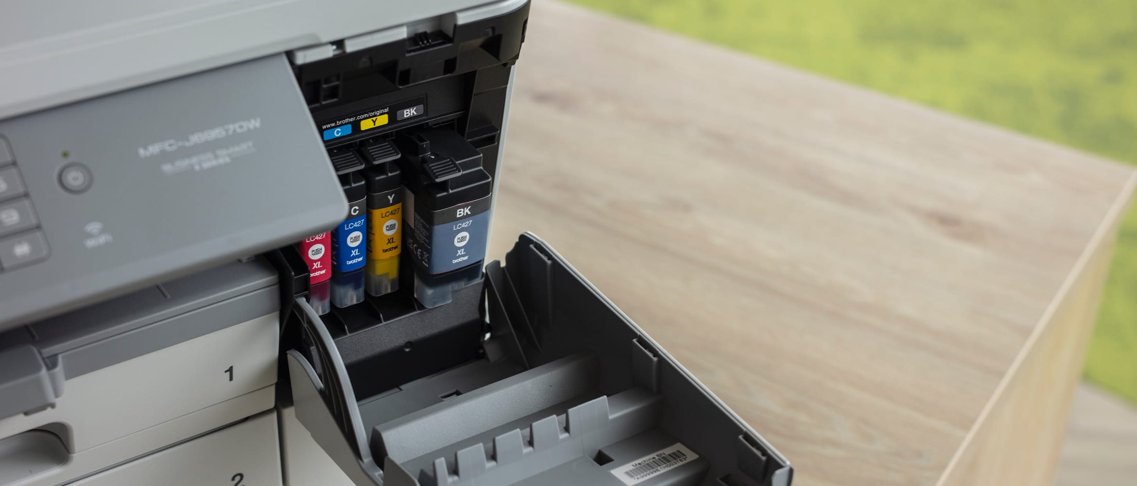 A Brother inkjet printer on a wooden table with it's supplies door open to reveal colour ink cartridges