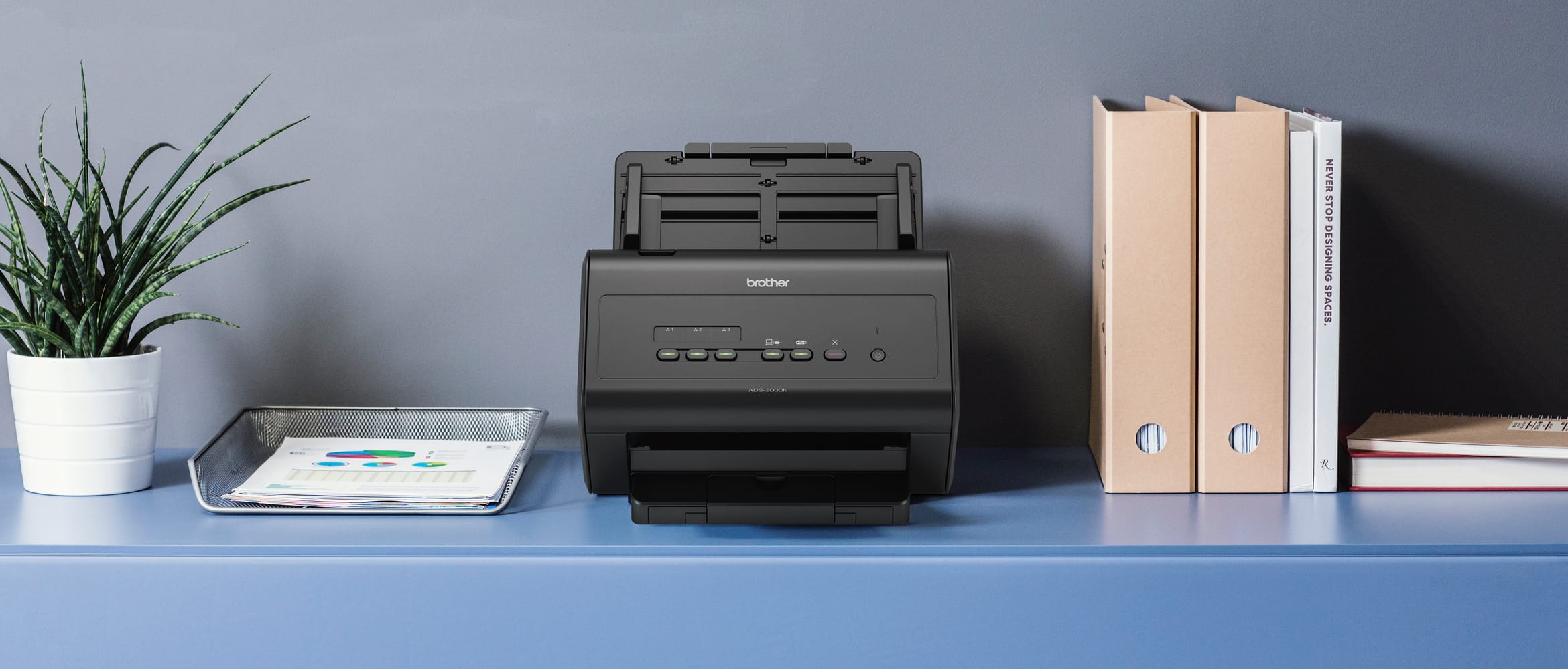 Brother ADS-3000N double-sided scanner on a blue sideboard next to folders, document tray and green plant