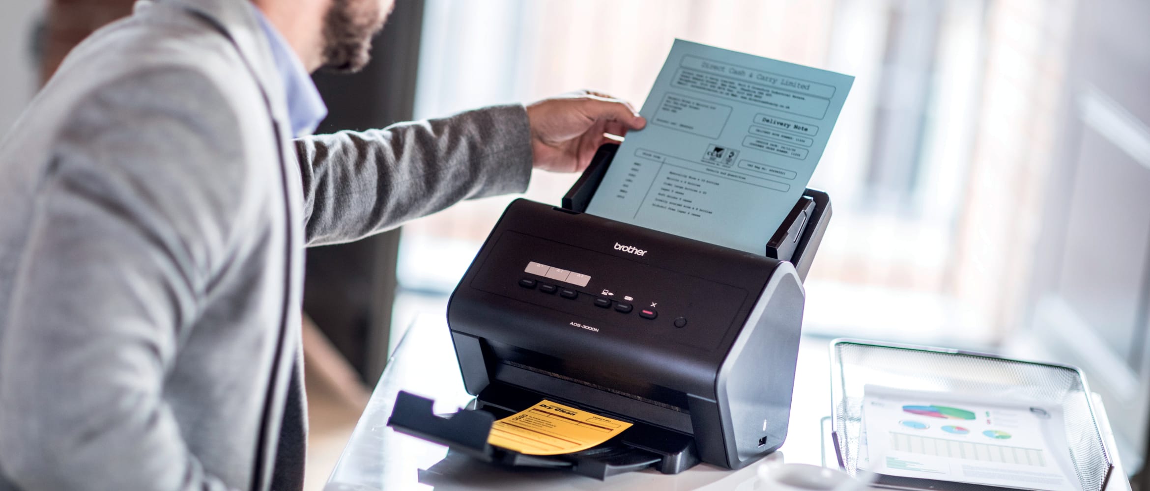 Man adding a document to the input tray of a Brother ADS-3000N sheetfed desktop scanner in a home office environment