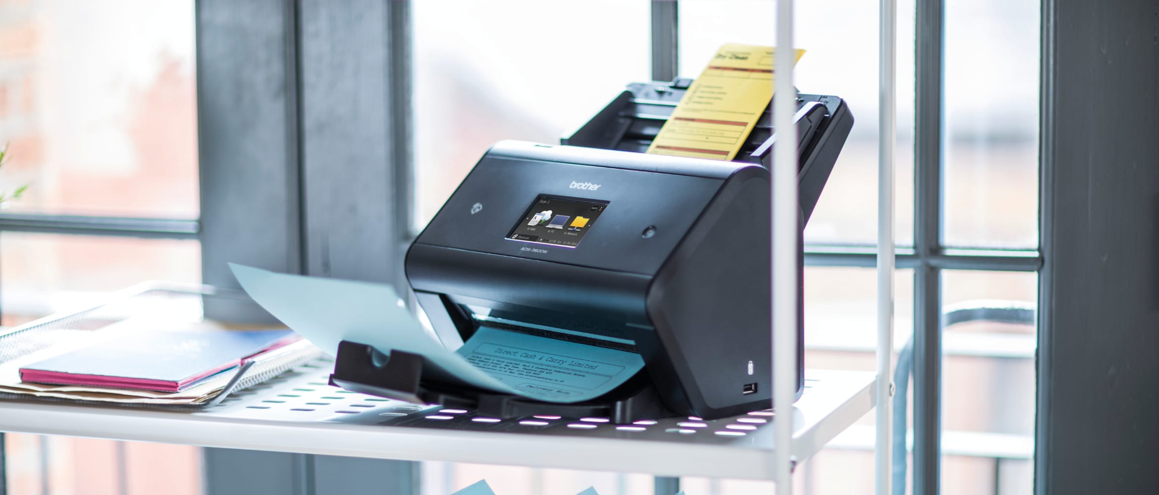 Brother ADS-3600W wireless scanner on a metal frame shelving unit in front of double glass doors