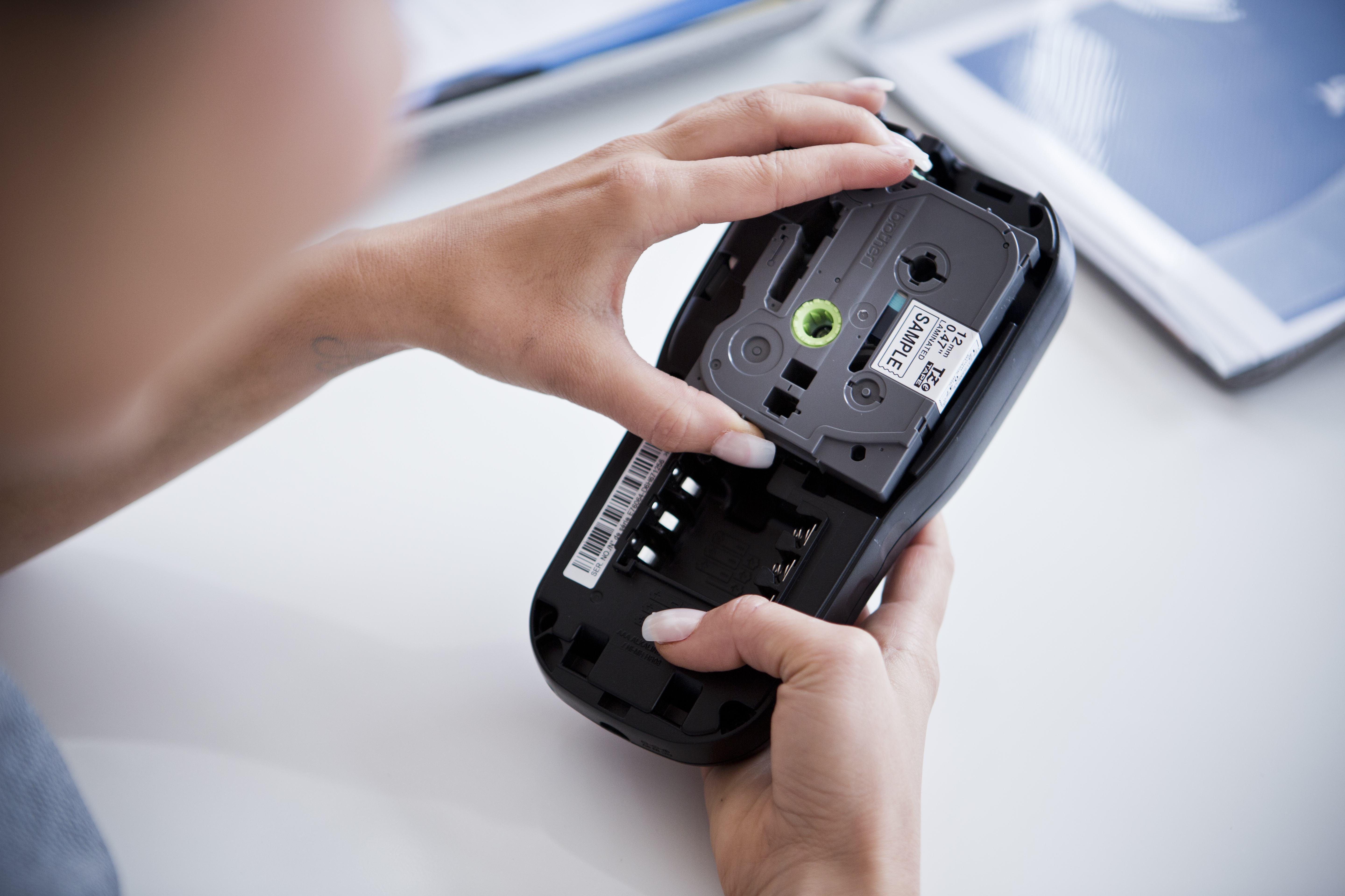 Image of a woman with long manicured nails fitting a tape cartridge into her PT labelling machine. 
