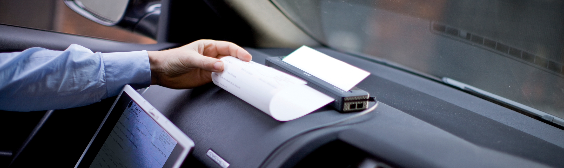 Man using a Brother PocketJet mobile printer on a car dashboard
