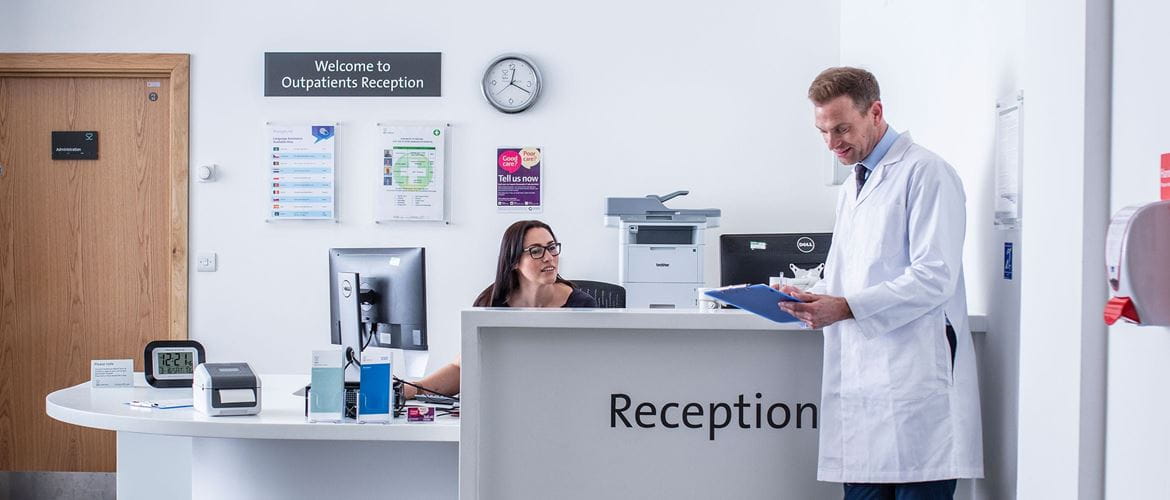 Hospital reception with female receptionist talking to doctor in white coat